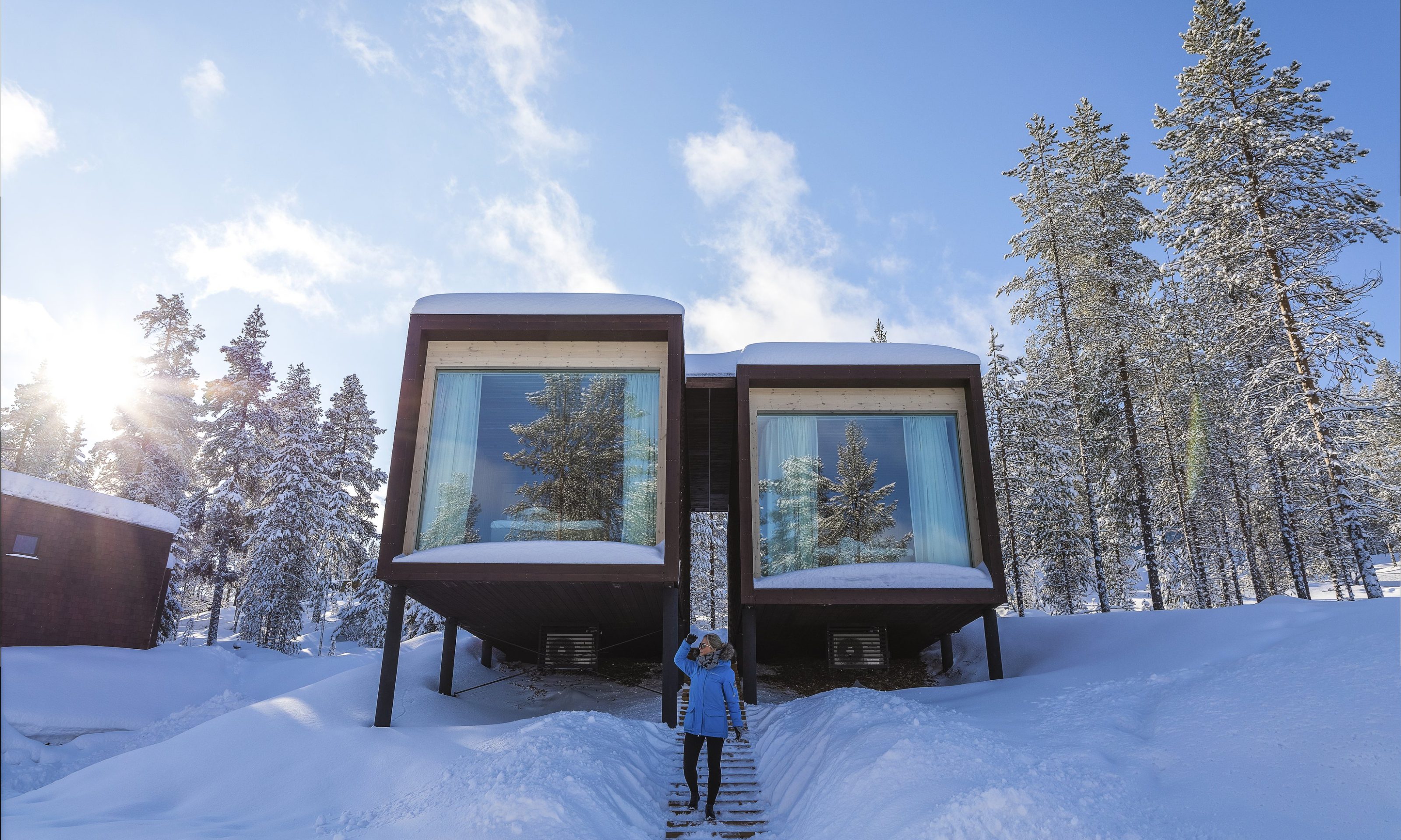 Woman standing front of the Arctic TreeHouse Hotel suite in sunny winter day.