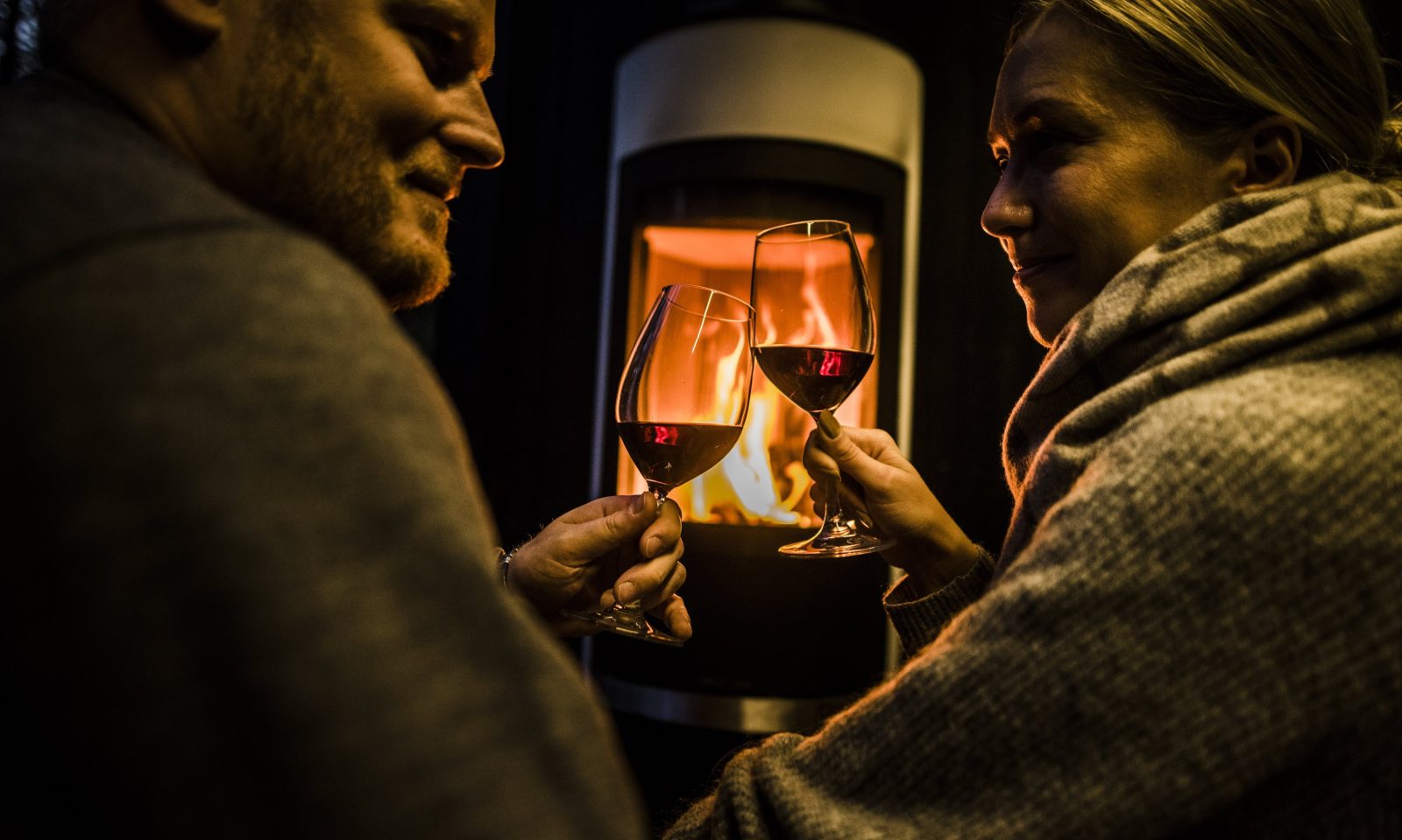 Couple enjoying red wine and warmth of fireplace in arctic scene executive suite.