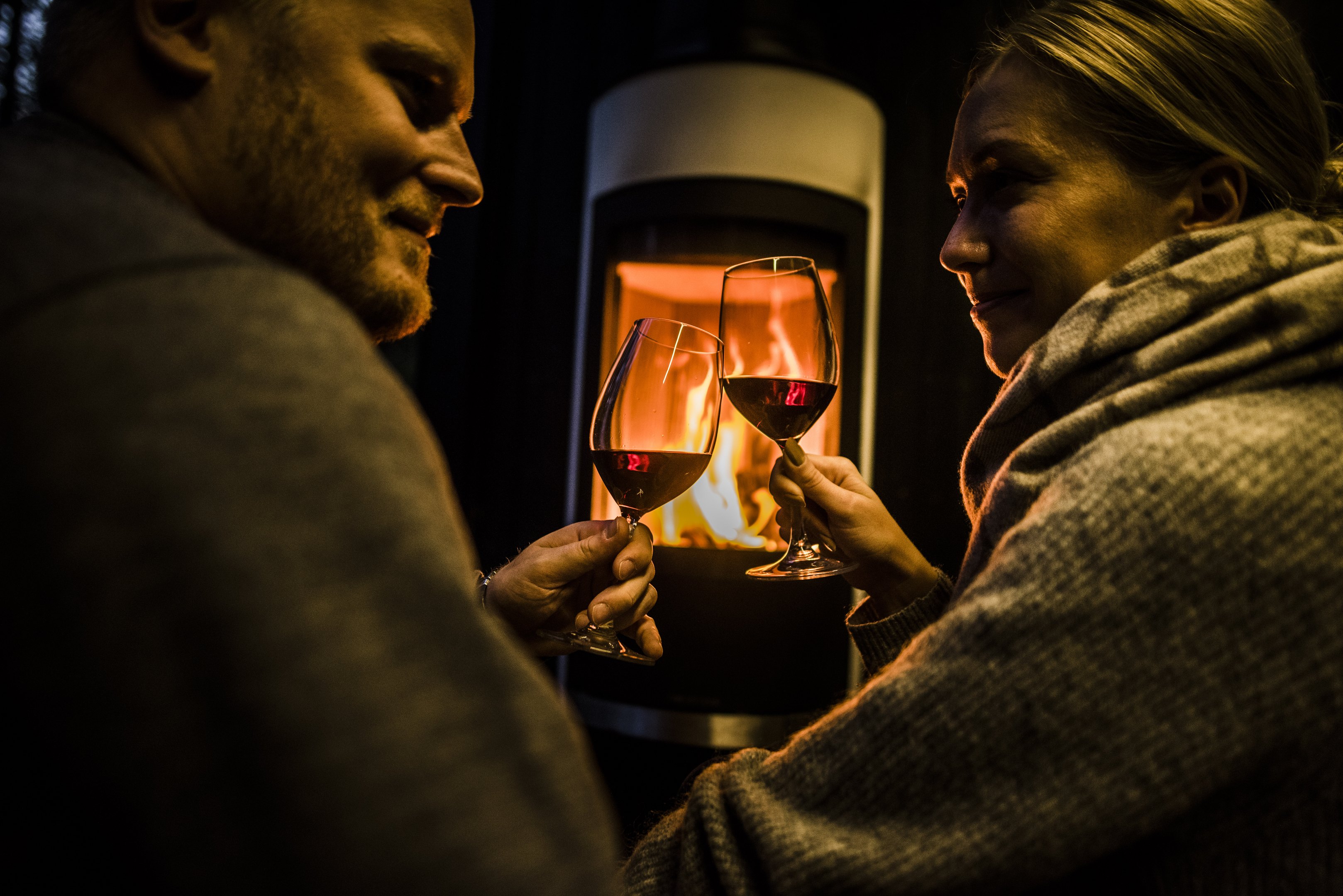 Couple enjoying red wine and warmth of fireplace in arctic scene executive suite.