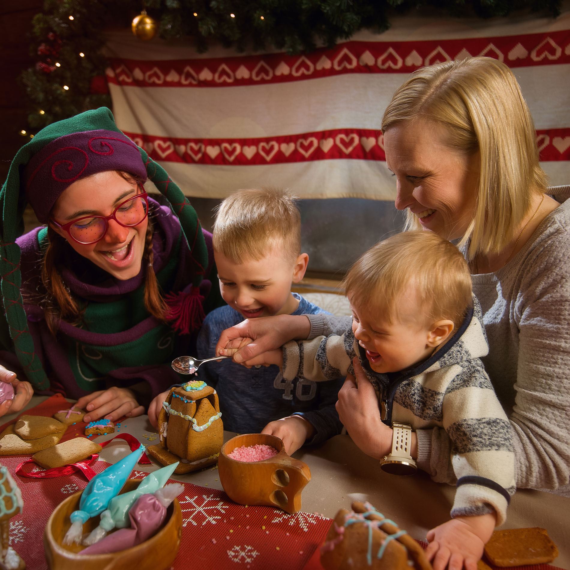Tonttu opettaa lapsia ja äitiä koristelemaan pientä piparkakkutaloa. | Santa Claus Secret Forest Joulukka