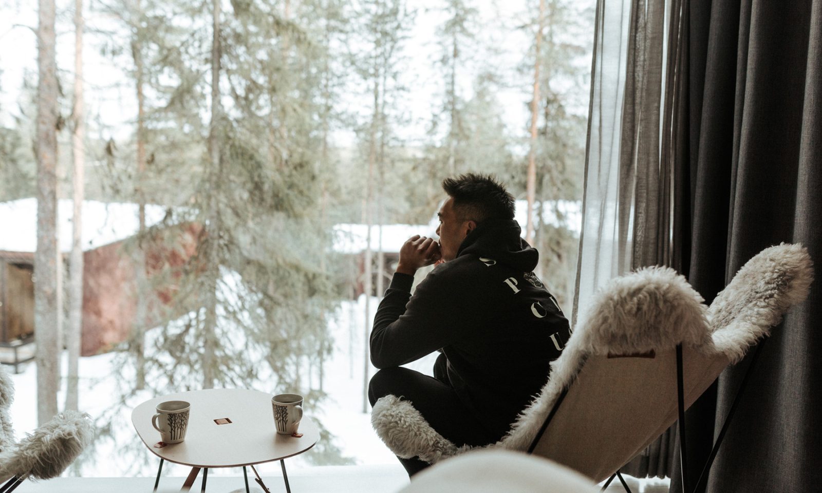 Man relaxing at the Arctic TreeHouse Hotel by the panoramic window with the view to the forest.