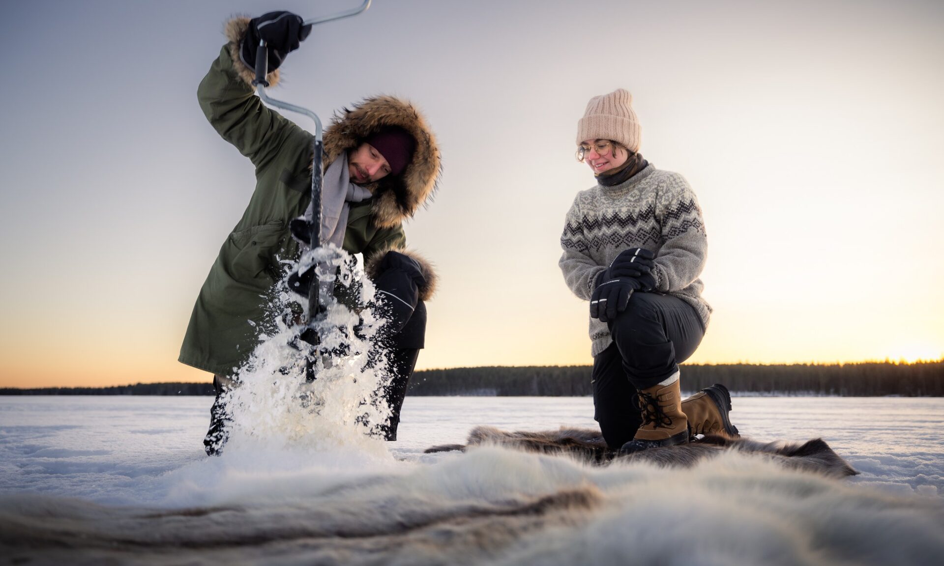 Couple experiencing Ice-fishing in the Lappish nature. Rovaniemi, Lapland, Finland. | Arctic TreeHouse Hotel