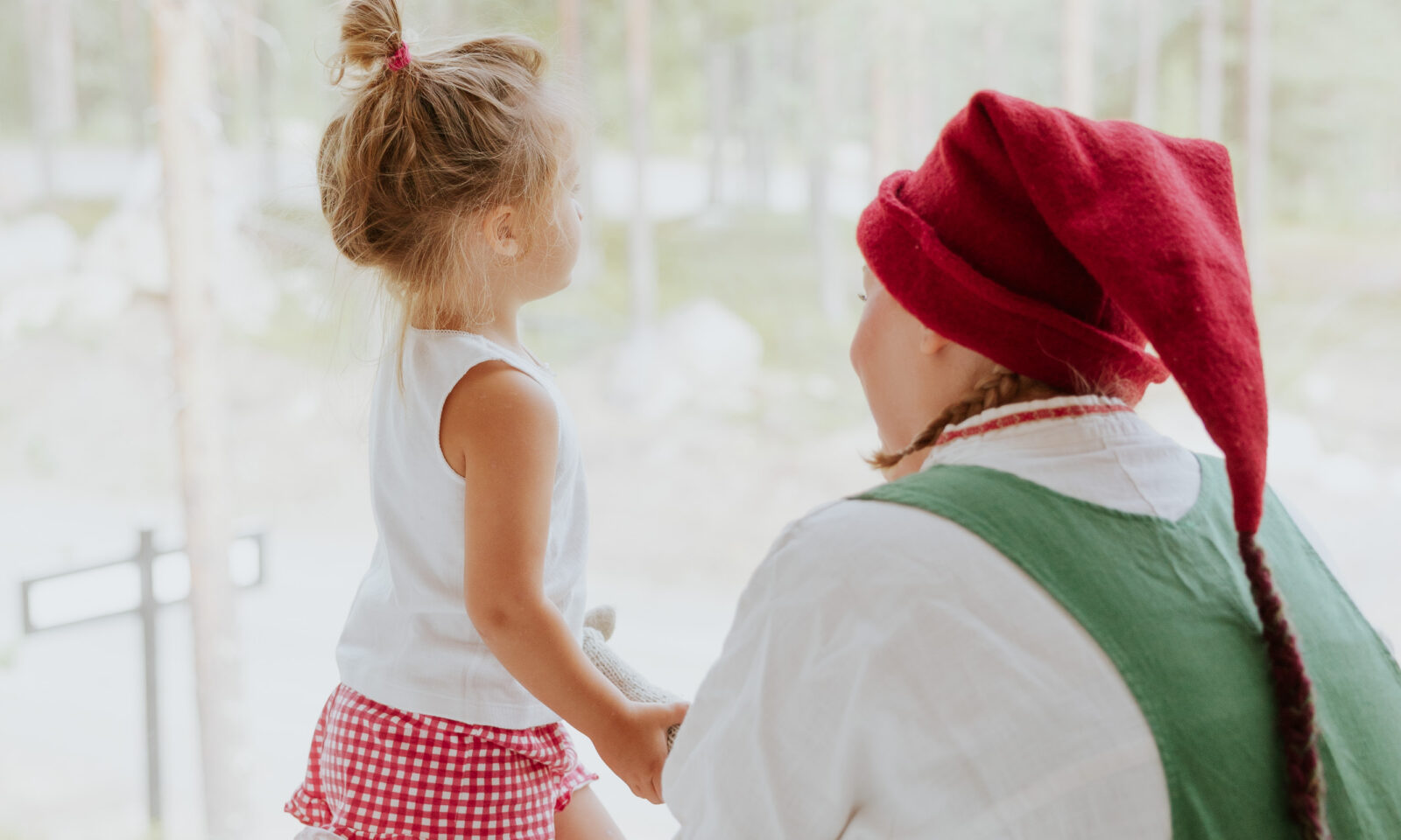 A child spending time with an Elf beside the panoramic window of an Arctic TreeHouse Hotel suite.