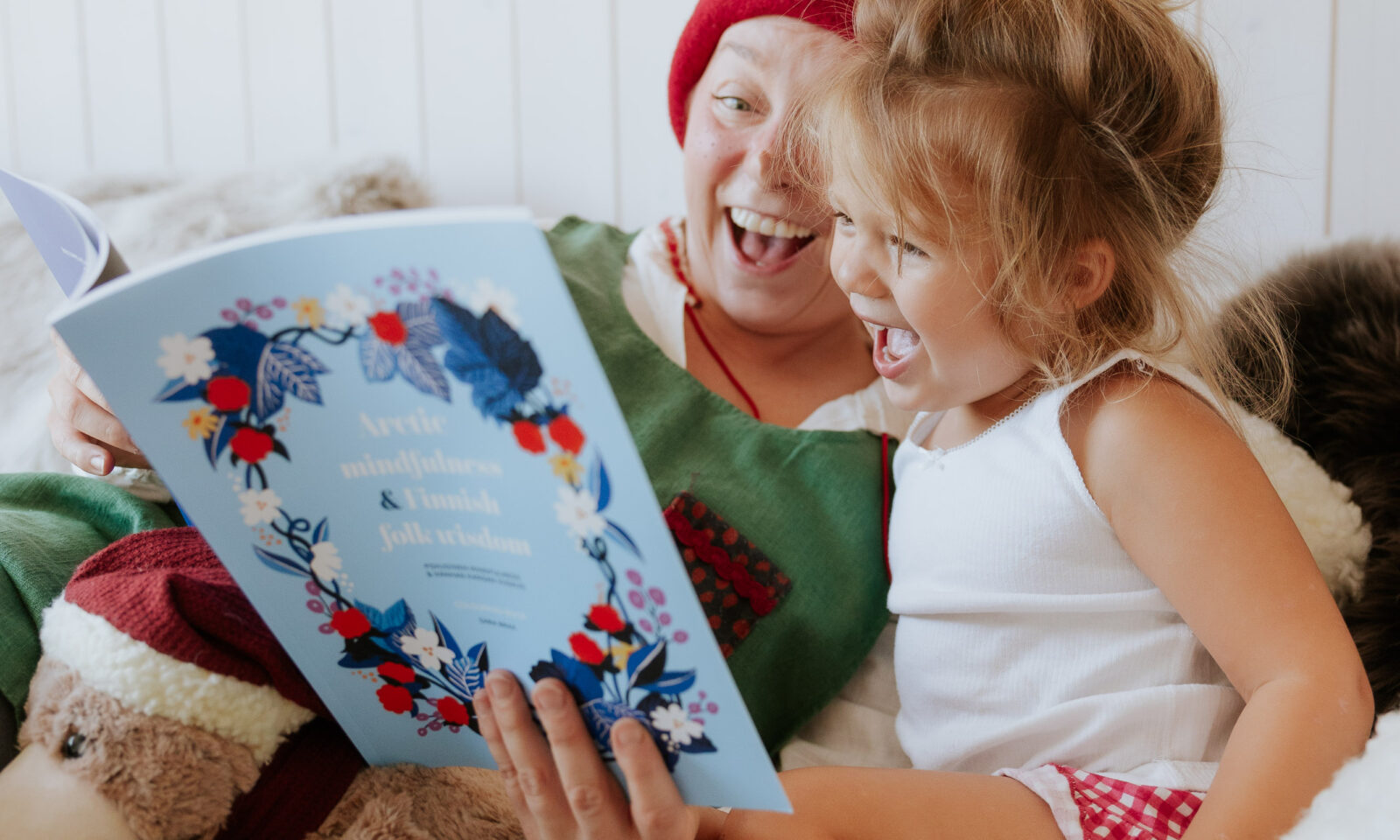 An Elf reading a storybook with a child on the bed at Arctic TreeHouse Hotel in Lapland.